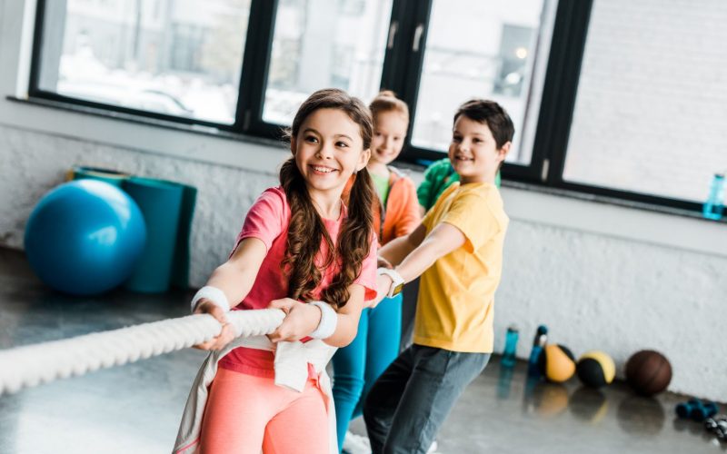 Smiling kids in sportswear pulling rope in gym