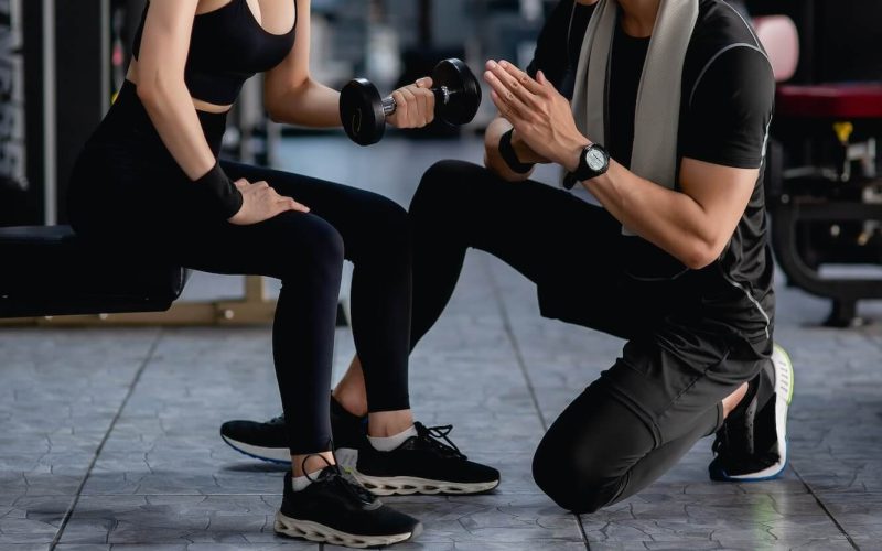 young-fitness-woman-exercise-with-dumbbell-by-trainer-in-gym-.jpg